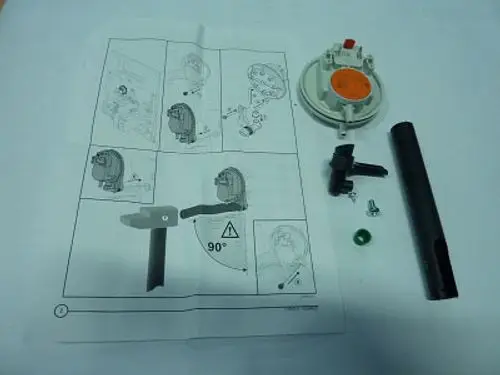 Remeha Luftdruckwächter mit Zubehörteilen und Montageanleitung auf Papier, inklusive einem schwarzen Rohr, einer grünen Kugel und weiteren Bestandteilen.